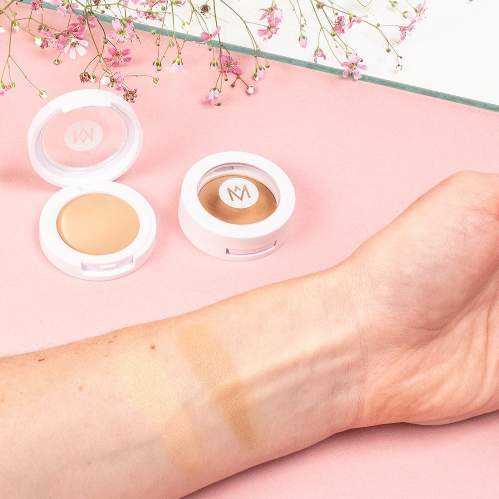 Deux boîtiers de correcteur blancs ronds. Ouvert et fermé. Bras avec deux échantillons de couleur. Fond rose.