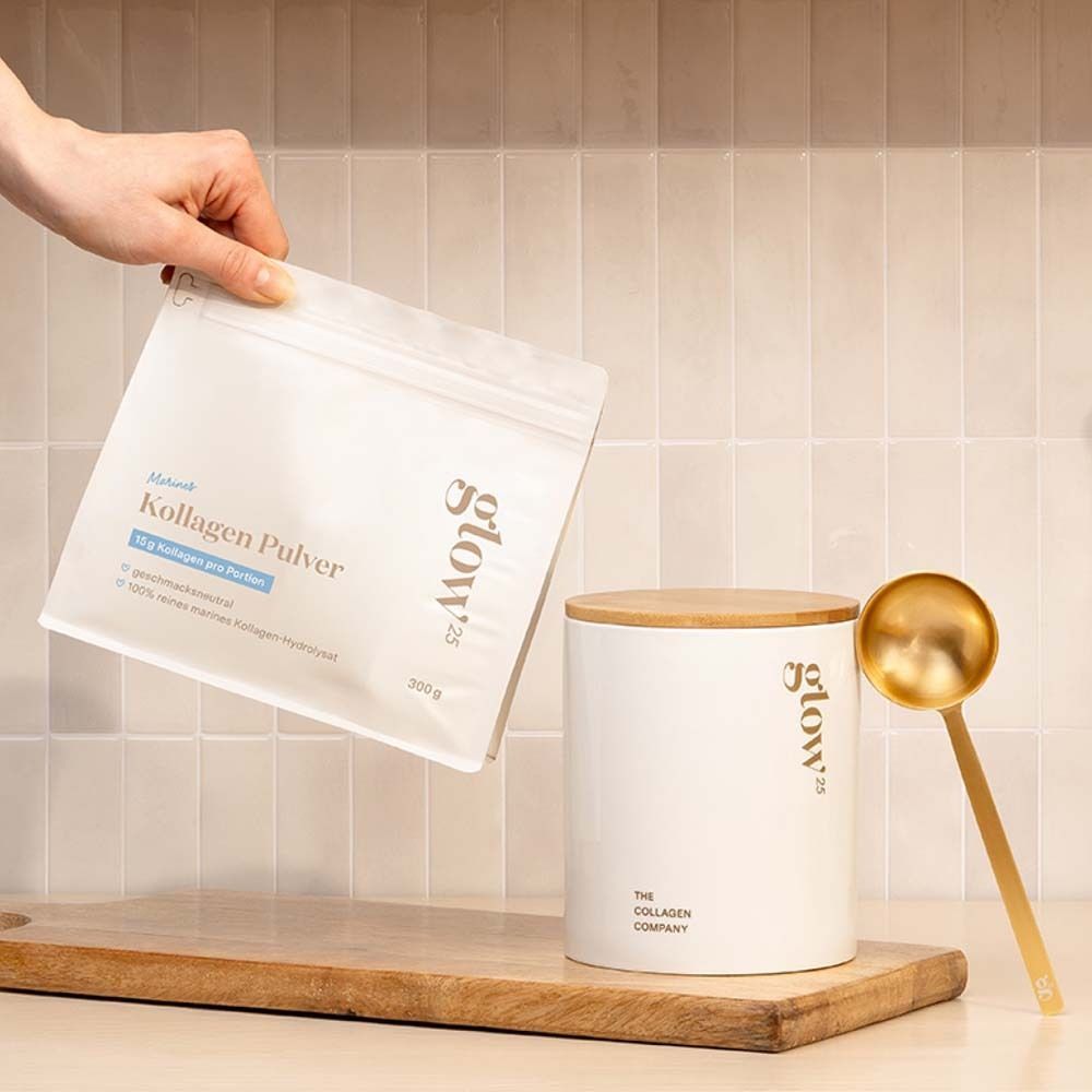 Main tenant un sachet blanc de poudre de collagène. À côté, un récipient blanc avec couvercle en bois et cuillère dorée. Inscription: Glow25.