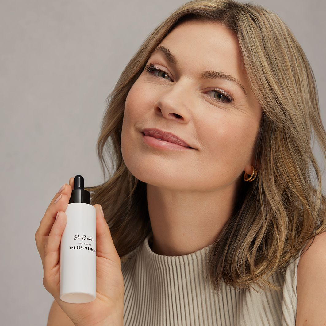 Frau hält eine weiße Flasche mit schwarzem Deckel. Aufschrift: Dr. Bouhon, THE SERUM ESSENCE.
