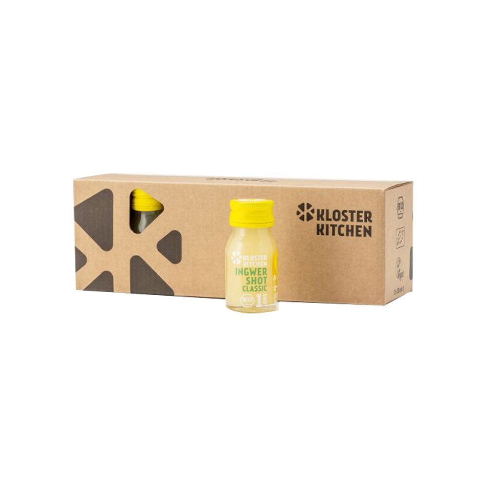 Eine Flasche Ingwer Shot Classic steht vor einer braunen Kartonverpackung mit dem Logo von Kloster Kitchen. Auf der Flasche steht Ingwer Shot Classic.