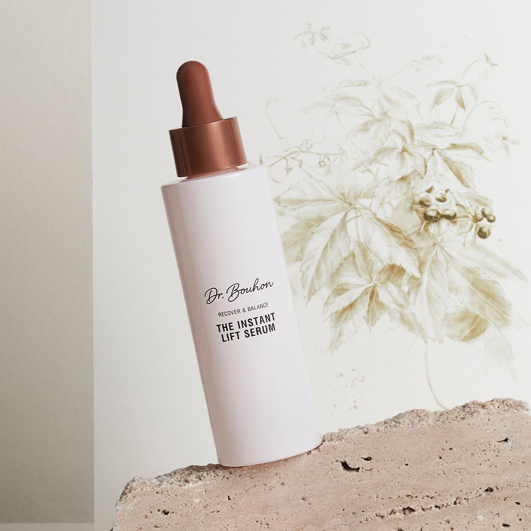 Rosa Flasche mit braunem Deckel auf Stein. Aufschrift: Dr. Bouhon, THE INSTANT LIFT SERUM. Hintergrund: Pflanze.