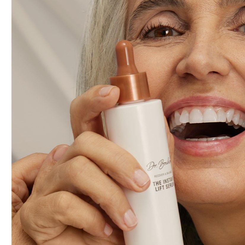 Frau hält rosa Flasche mit braunem Deckel. Aufschrift: Dr. Bouhon, THE INSTANT LIFT SERUM. Frau lächelt.
