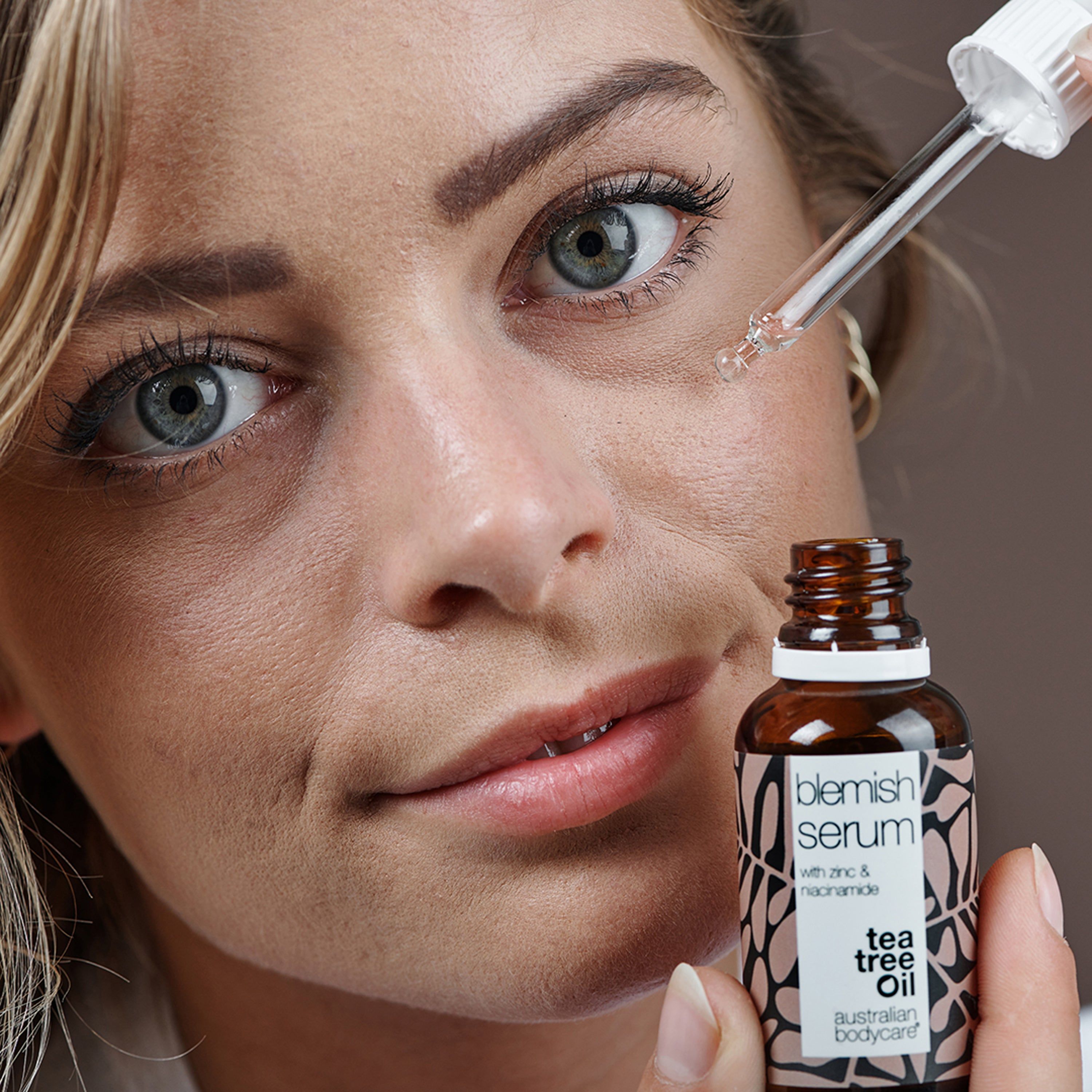 Femme avec pipette et flacon de Blemish Serum. Inscription : Blemish Serum, Tea Tree Oil. Marque : Australian Bodycare.