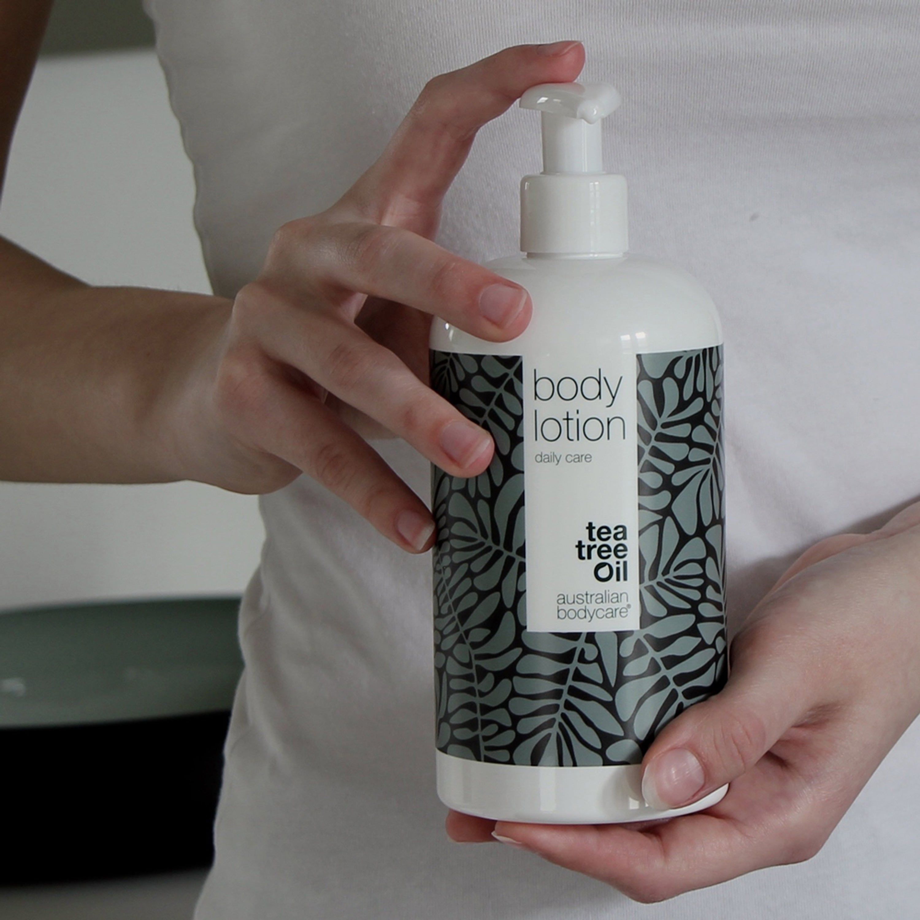 Flacon blanc avec pompe. Inscription : body lotion, daily care. Logo : Australian Bodycare. Mains tenant le flacon.