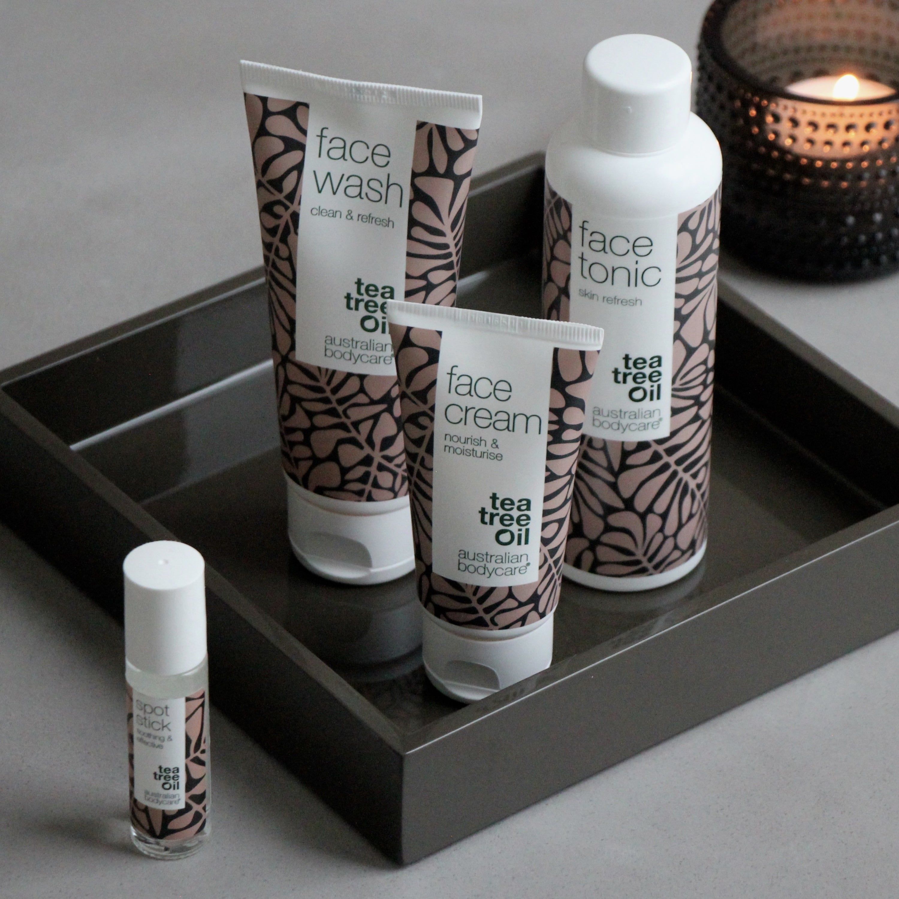 Set mit Face Wash, Face Tonic, Face Cream und Spot Stick auf Tablett. Verpackung mit braunen Blättern. Text: Tea Tree Oil, Australian Bodycare.