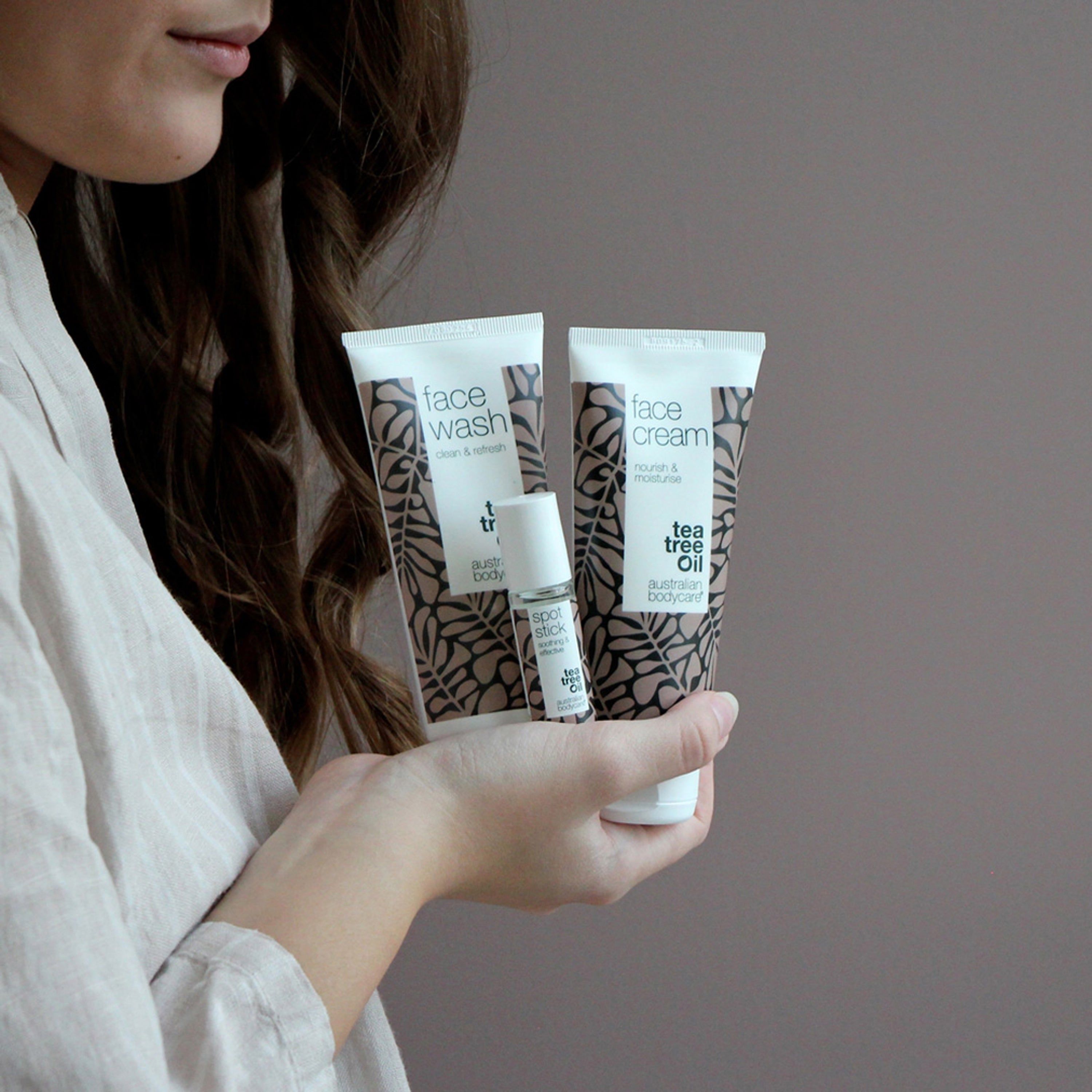 Person hält Face Wash, Face Cream und Spot Stick. Verpackung mit braunen Blättern. Text: Australian Bodycare.